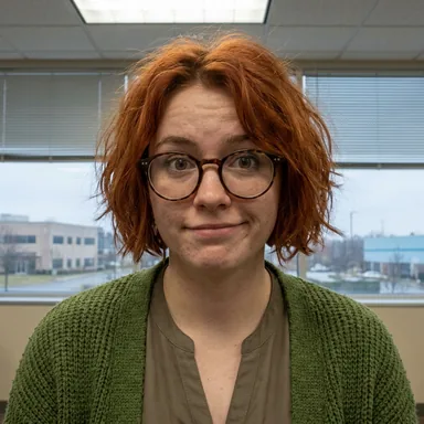 Workplace mockumentary office portrait photo of a young woman with a copper-red bob and round glasses